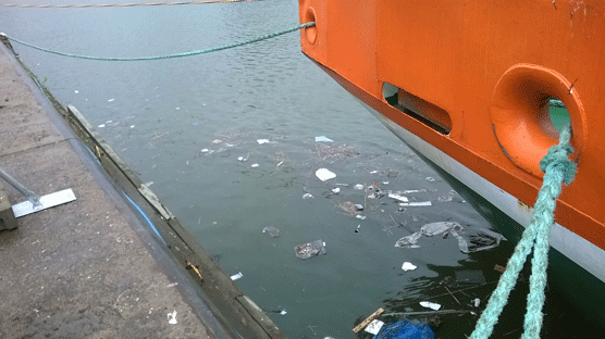 Plastic litter floating in the sea beside a ship.